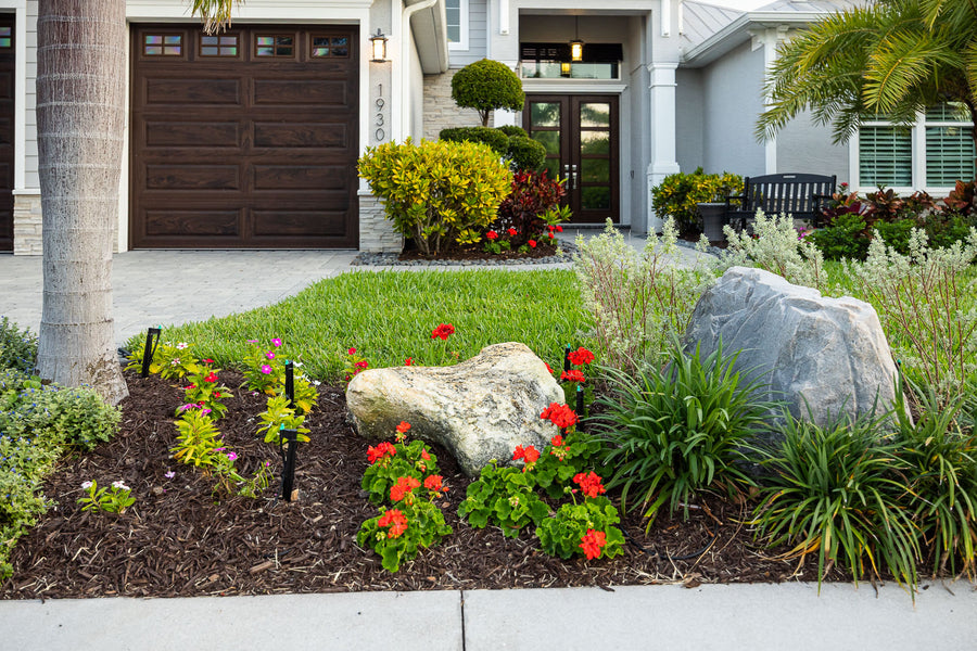 Layered tropical beds with decorative rock along a curved sidewalk